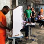 Urna eleitoral brasileira com grade de prisão ao fundo, simbolizando suspensão do voto de presos