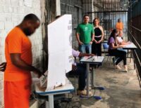 Urna eleitoral brasileira com grade de prisão ao fundo, simbolizando suspensão do voto de presos